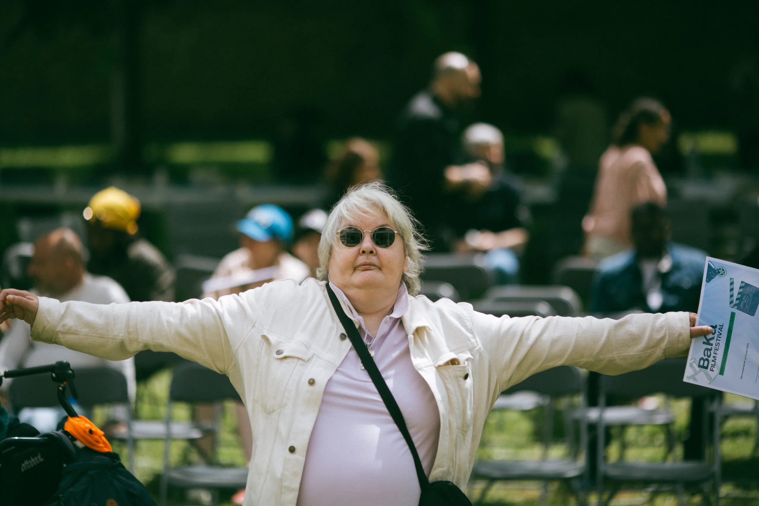 Une femme aux lunettes de soleil ouvre grand les bras devant un public assis en plein air